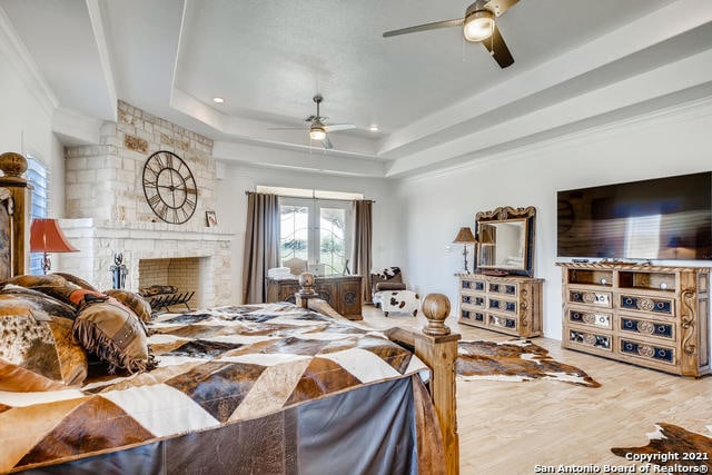 bedroom featuring hardwood / wood-style floors, ceiling fan, a tray ceiling, a brick fireplace, and french doors