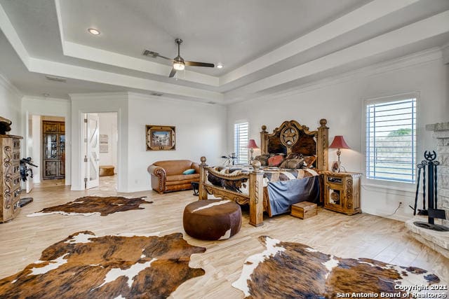 bedroom with ornamental molding, ensuite bathroom, ceiling fan, and a tray ceiling