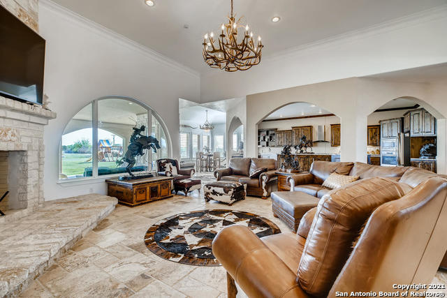 living room featuring a stone fireplace, ornamental molding, a chandelier, and a towering ceiling