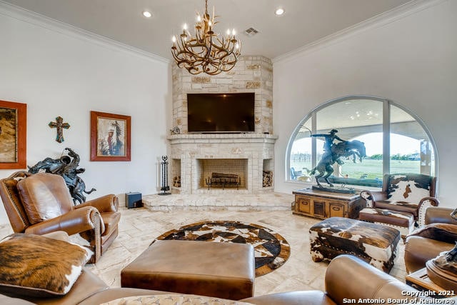 living room featuring crown molding, a stone fireplace, a chandelier, and a high ceiling