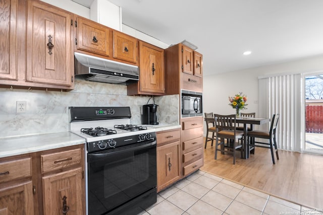 kitchen featuring light tile patterned flooring, tasteful backsplash, gas range oven, and black microwave