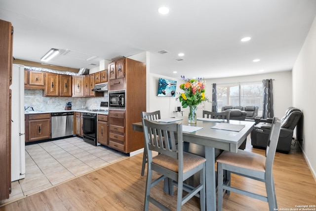 kitchen with black microwave, backsplash, stainless steel dishwasher, gas stove, and light hardwood / wood-style flooring