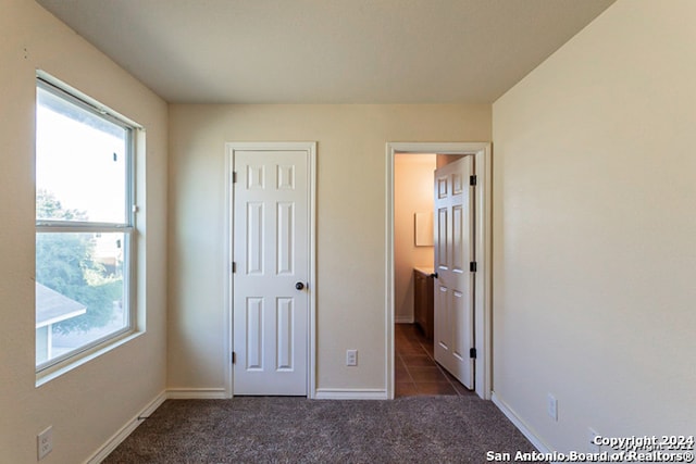 unfurnished bedroom featuring connected bathroom and dark carpet