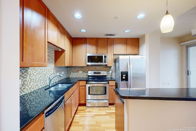 kitchen with sink, appliances with stainless steel finishes, hanging light fixtures, decorative backsplash, and light wood-type flooring