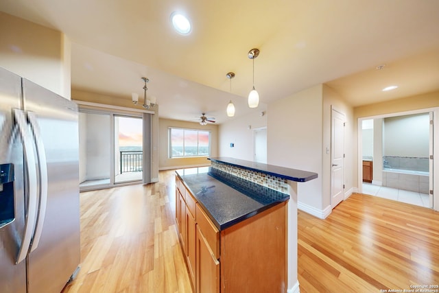 kitchen featuring a kitchen island, ceiling fan with notable chandelier, pendant lighting, stainless steel fridge, and light wood-type flooring