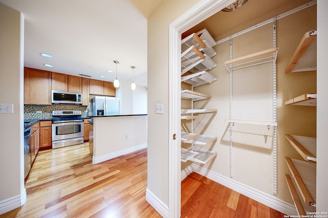 kitchen with hanging light fixtures, appliances with stainless steel finishes, light hardwood / wood-style floors, and decorative backsplash