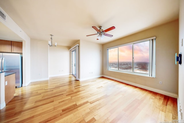 unfurnished living room featuring ceiling fan with notable chandelier and light hardwood / wood-style flooring