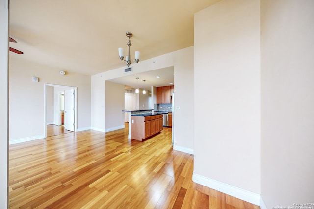 kitchen with a kitchen island, ceiling fan with notable chandelier, tasteful backsplash, hanging light fixtures, and light hardwood / wood-style floors