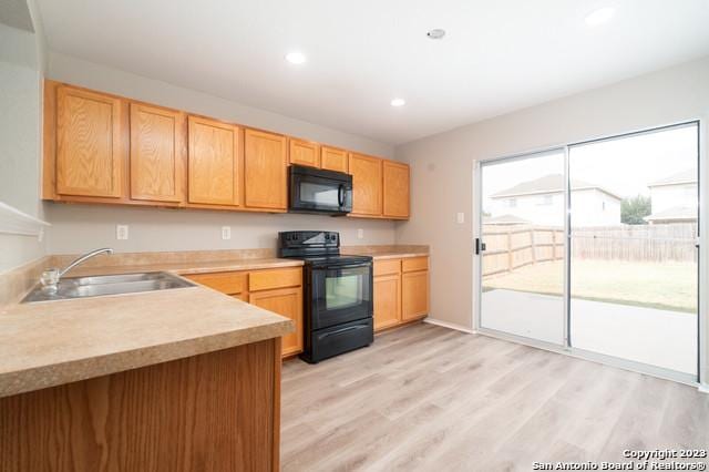 kitchen featuring light brown cabinetry, sink, black appliances, and light wood-type flooring