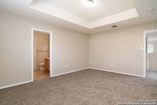 unfurnished bedroom with ensuite bathroom, a raised ceiling, and carpet flooring