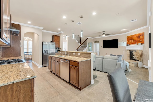 kitchen with appliances with stainless steel finishes, pendant lighting, sink, light stone countertops, and a center island with sink