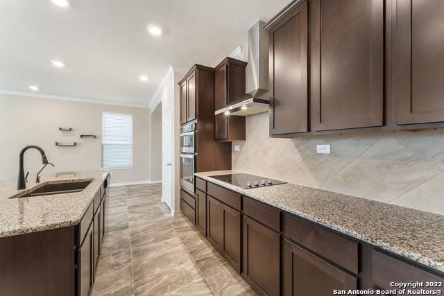 kitchen featuring sink, dark brown cabinets, black electric stovetop, light stone countertops, and wall chimney range hood