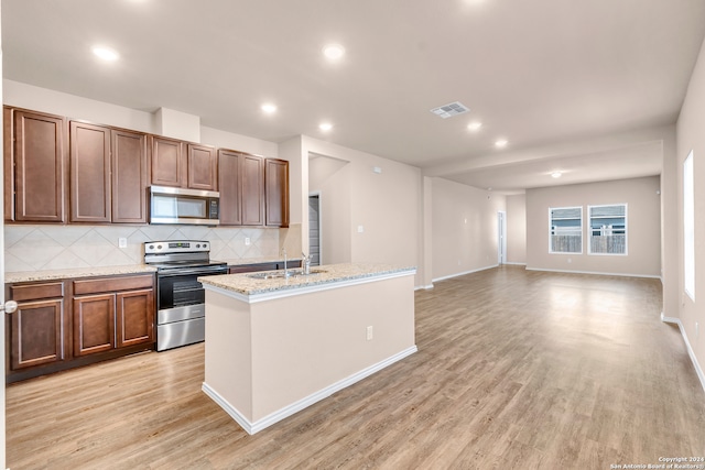 kitchen with appliances with stainless steel finishes, sink, a center island with sink, and light wood-type flooring