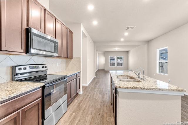 kitchen with appliances with stainless steel finishes, sink, decorative backsplash, a kitchen island with sink, and light hardwood / wood-style flooring