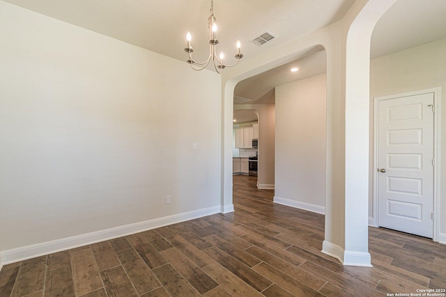 empty room with dark hardwood / wood-style floors and a notable chandelier