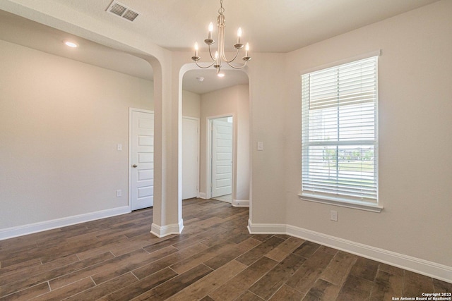 empty room with dark wood-type flooring and a notable chandelier