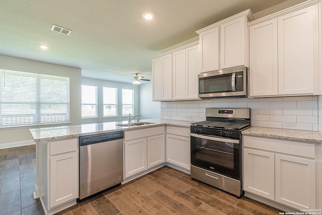 kitchen with sink, appliances with stainless steel finishes, white cabinetry, backsplash, and kitchen peninsula