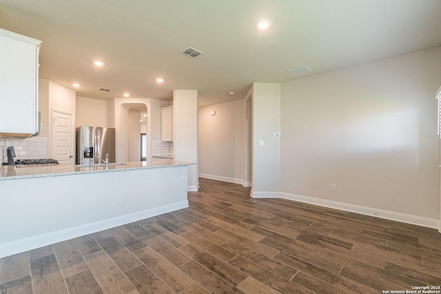 kitchen with white cabinets, backsplash, stainless steel fridge, dark hardwood / wood-style flooring, and light stone countertops