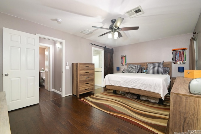 bedroom with a barn door, dark hardwood / wood-style floors, connected bathroom, and ceiling fan