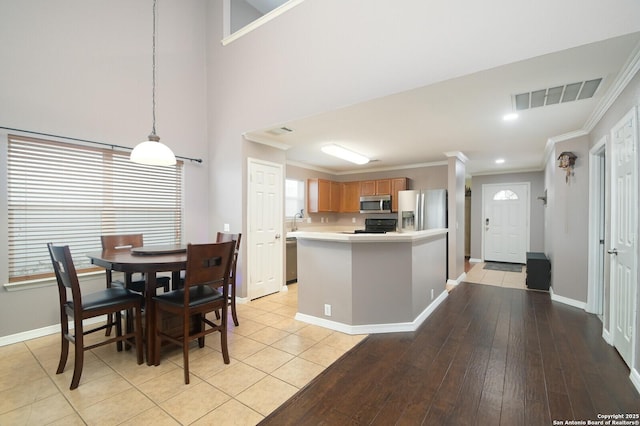 kitchen featuring decorative light fixtures, light hardwood / wood-style flooring, ornamental molding, appliances with stainless steel finishes, and a high ceiling