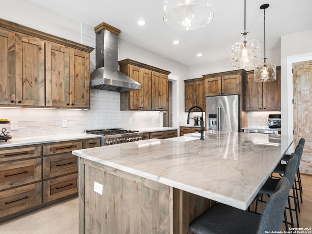 kitchen featuring pendant lighting, wall chimney range hood, stainless steel appliances, a spacious island, and a kitchen bar