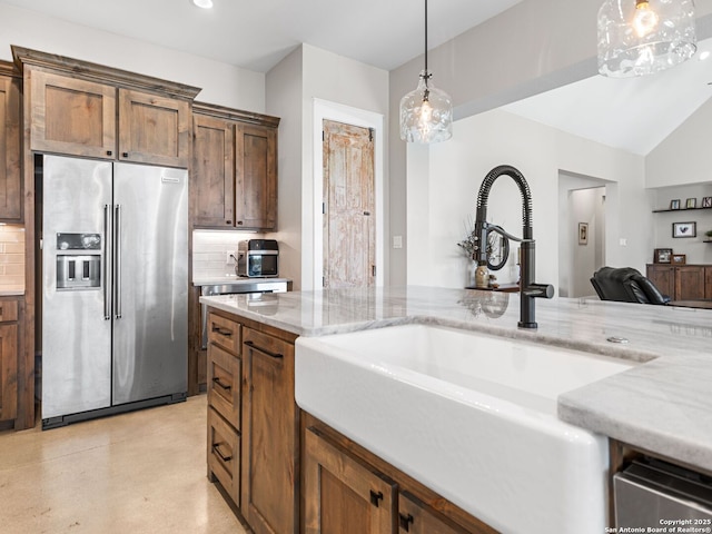 kitchen with high quality fridge, decorative light fixtures, sink, backsplash, and light stone counters