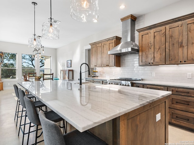 kitchen featuring sink, hanging light fixtures, backsplash, exhaust hood, and a large island with sink