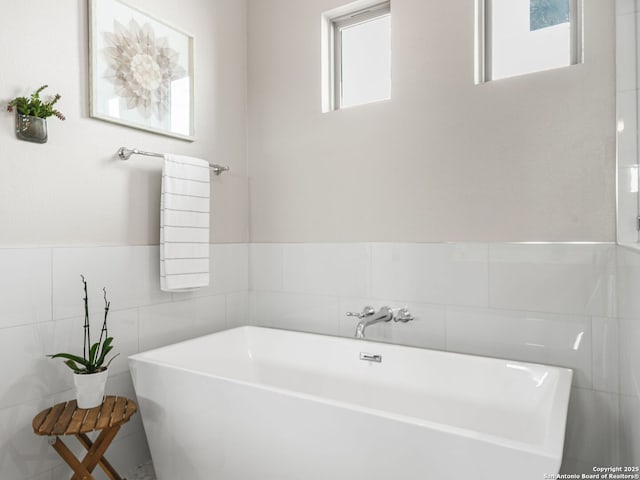 bathroom featuring tile walls, a bathing tub, and a healthy amount of sunlight