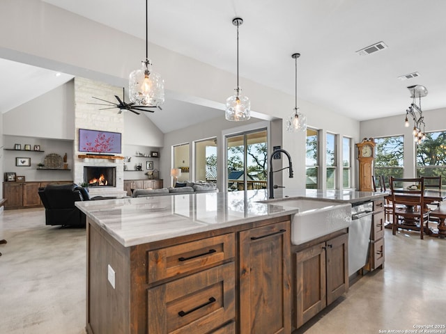 kitchen featuring sink, a kitchen island with sink, hanging light fixtures, a stone fireplace, and stainless steel dishwasher