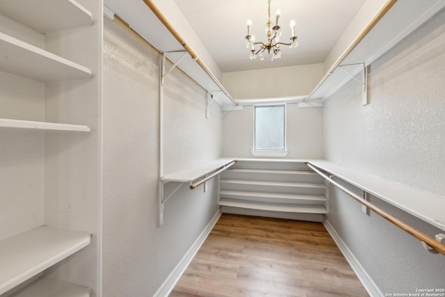 walk in closet with light hardwood / wood-style floors and a notable chandelier