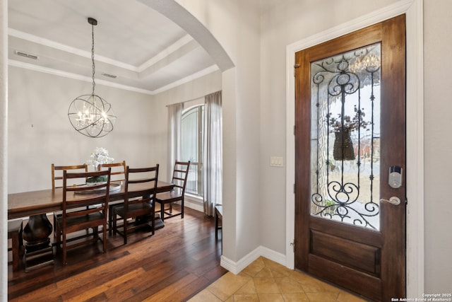 entryway with a notable chandelier, hardwood / wood-style flooring, ornamental molding, and a raised ceiling