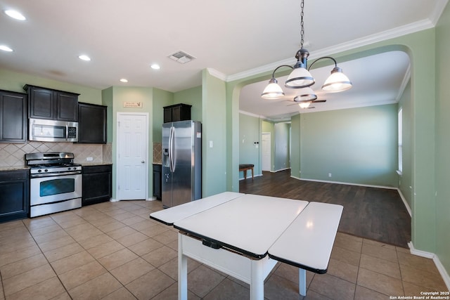 kitchen with pendant lighting, ornamental molding, stainless steel appliances, and light tile patterned floors