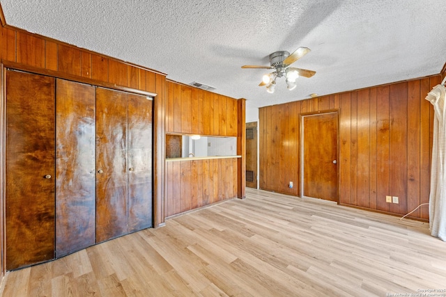 unfurnished bedroom with wood walls, a textured ceiling, light wood-type flooring, a closet, and ceiling fan