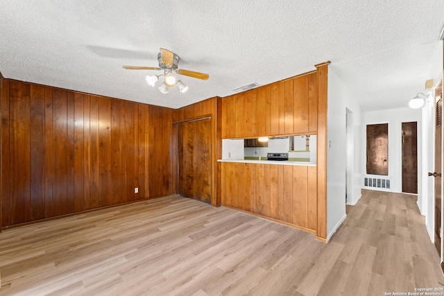 kitchen with stainless steel electric range, a textured ceiling, light wood-type flooring, wooden walls, and ceiling fan