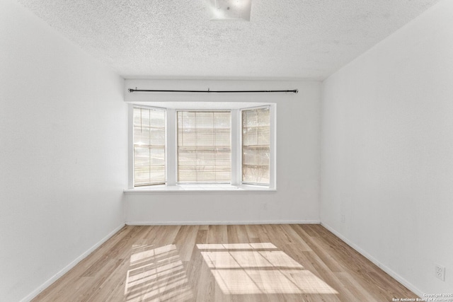 spare room featuring a textured ceiling, light hardwood / wood-style flooring, and a healthy amount of sunlight