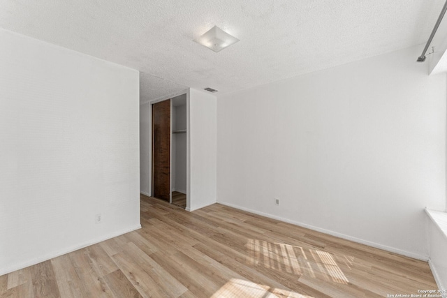 unfurnished room featuring a textured ceiling and light hardwood / wood-style flooring