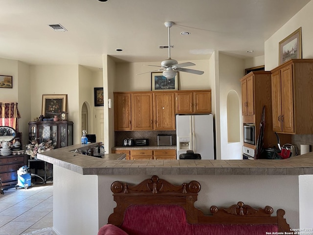 kitchen with a breakfast bar, stainless steel microwave, white fridge with ice dispenser, tile countertops, and kitchen peninsula