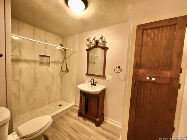 bathroom with hardwood / wood-style floors, a tile shower, a textured ceiling, and toilet