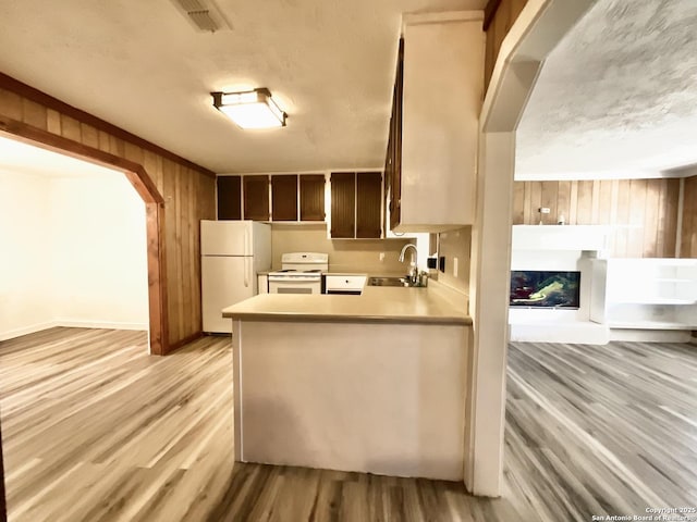 kitchen featuring sink, wooden walls, kitchen peninsula, white appliances, and light hardwood / wood-style floors