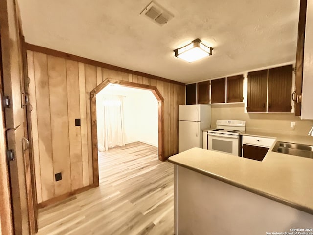 kitchen featuring sink, wood walls, dark brown cabinets, kitchen peninsula, and white appliances