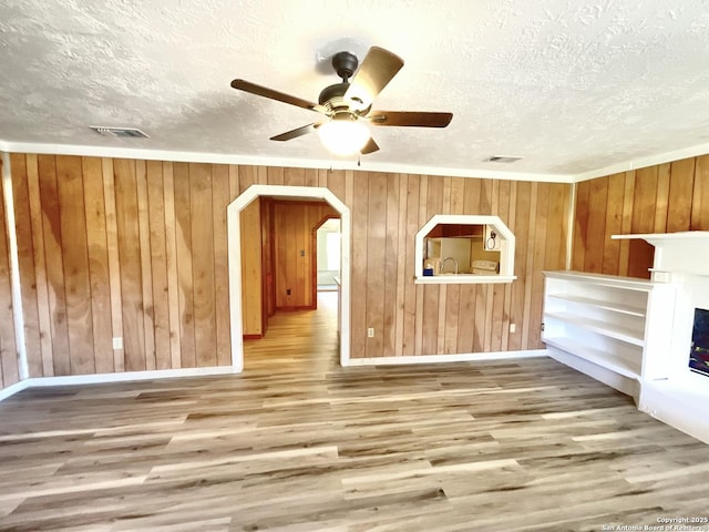 unfurnished living room with ceiling fan, hardwood / wood-style floors, a textured ceiling, and wood walls