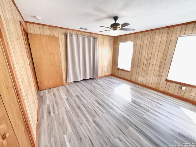 spare room featuring ornamental molding, wood walls, ceiling fan, and light wood-type flooring