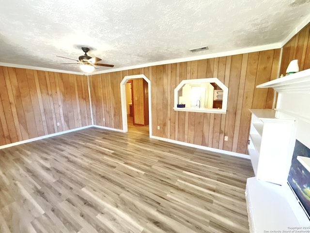 unfurnished living room featuring wood-type flooring, ceiling fan, a textured ceiling, and wood walls