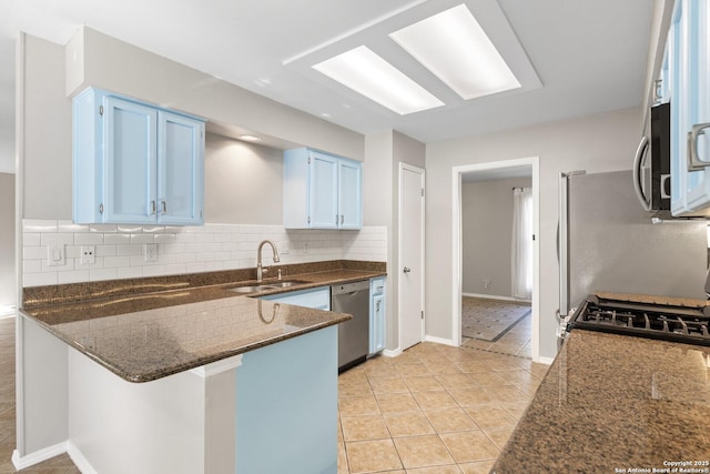 kitchen with appliances with stainless steel finishes, blue cabinets, sink, dark stone counters, and decorative backsplash