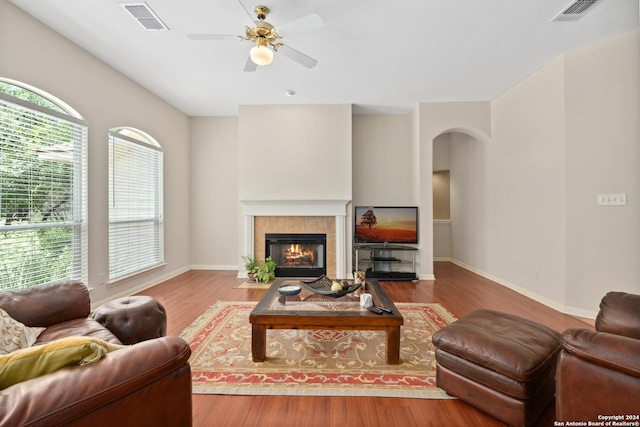 living room with a tiled fireplace, wood-type flooring, and ceiling fan