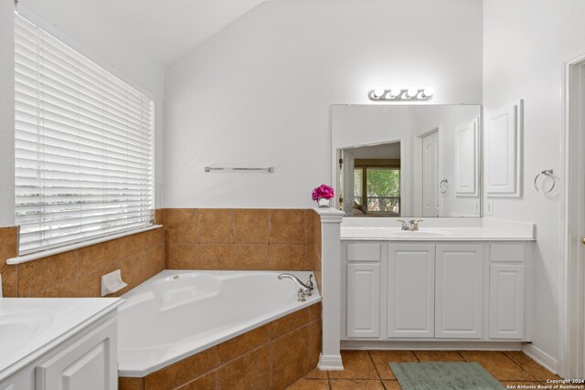 bathroom with lofted ceiling, tiled tub, vanity, and tile patterned floors