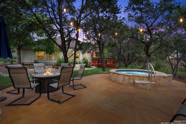 patio terrace at dusk featuring a wooden deck, a fire pit, and an in ground hot tub