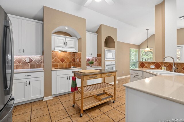kitchen featuring lofted ceiling, sink, white appliances, white cabinetry, and decorative light fixtures