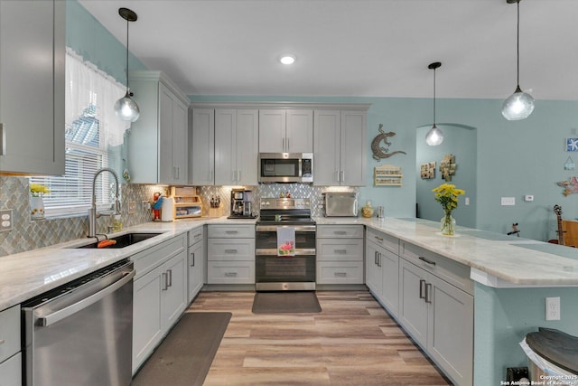 kitchen featuring sink, stainless steel appliances, light stone counters, decorative light fixtures, and kitchen peninsula