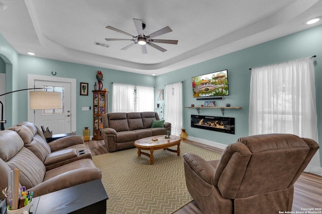 living room featuring ceiling fan, light hardwood / wood-style floors, and a tray ceiling